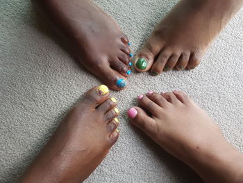 Low section of female friends with colorful nail polishes on carpet