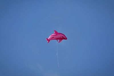 Low angle view of red paragliding against clear blue sky