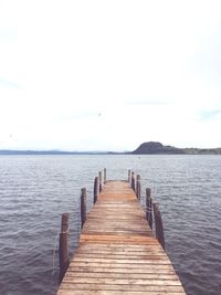 Wooden jetty leading to pier over sea against sky