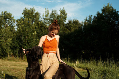 Woman riding dog on field against trees