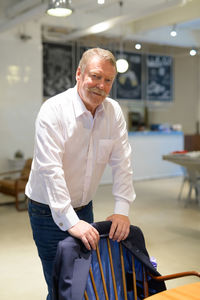 Portrait of smiling senior man standing by chair