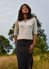 Low angle portrait of young woman standing on grassy field