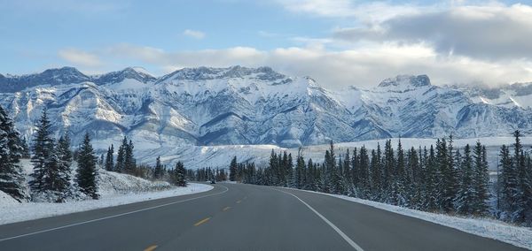 Road amidst snowcapped mountains against sky during winter