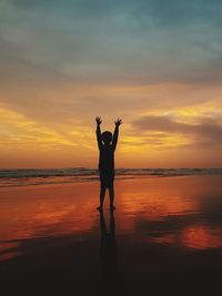 Silhouette woman standing on beach against sky during sunset