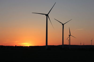 Silhouette wind turbines on field against sky during sunset