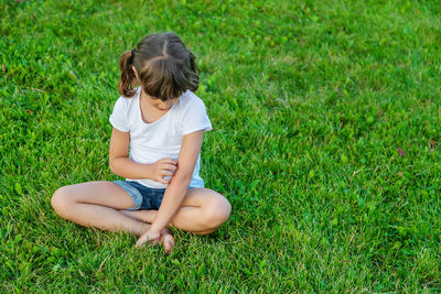 Cute girl scratching hand while sitting on grass