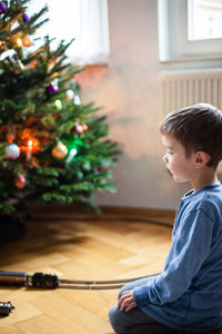 Side view of boy sitting at christmas tree