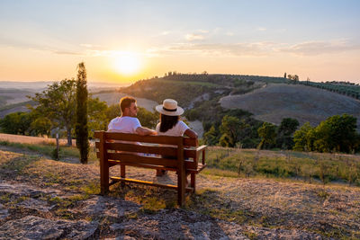 Rear view of people sitting on bench looking at sunset