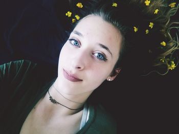 High angle portrait of young woman with flowers in hair lying on bed