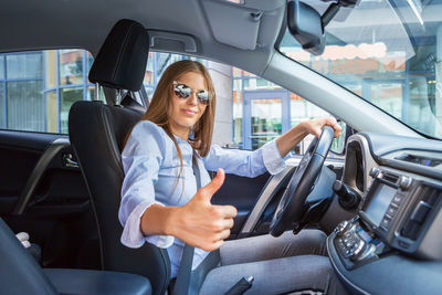 Portrait of young woman showing thumbs up while driving car