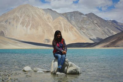 Young woman sitting on lake against mountains