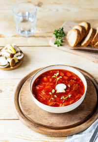 Vegan beetroot soup with mushrooms in a bowl, bread, glass of water on a wooden background