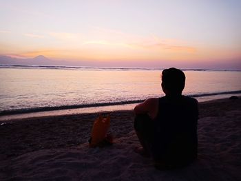 Rear view of woman sitting on beach during sunset