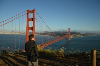 Rear view of man standing by golden gate bridge over san francisco bay