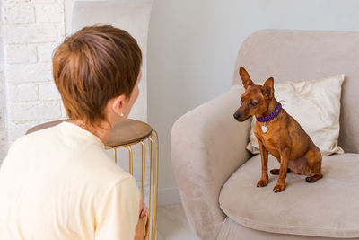 Owner playing with joyful dog at home, happy mature woman enjoying exercise