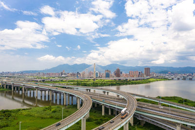 Bridge over road by buildings in city against sky