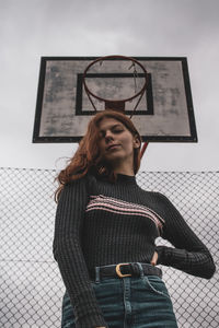 Low angle view portrait of woman standing against basketball hoop