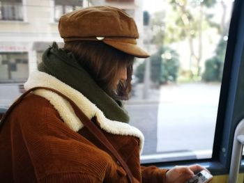 Side view of woman wearing warm clothing while using mobile phone in bus