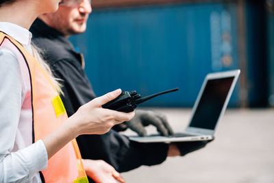 Midsection of woman holding walkie-talkie by man using laptop