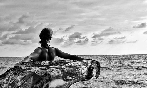 Rear view of young woman sitting against sea