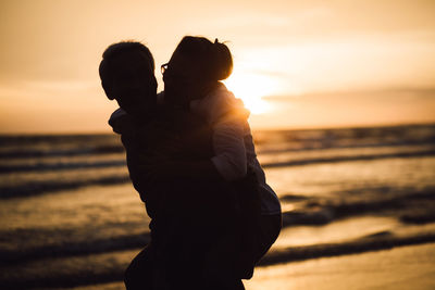 Rear view of couple standing at beach during sunset