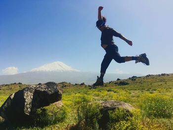 Man with arms raised on rock against sky