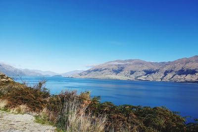 Scenic view of lake by mountains against clear blue sky