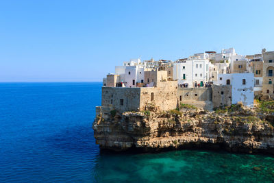 Buildings by sea against clear blue sky