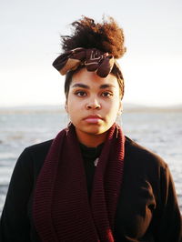 Portrait of young woman standing at beach against sky