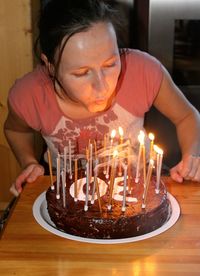 Woman blowing lit candles on birthday cake at table