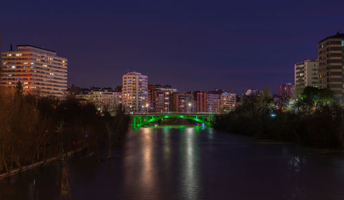 Illuminated buildings by river against sky in city at night