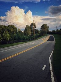 Road amidst trees against cloudy sky