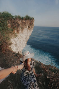 Woman hand on rock by sea against sky