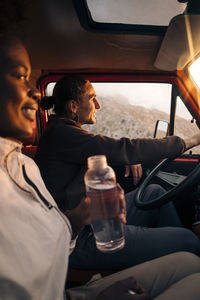 Young man driving van while sitting with female friend holding water bottle