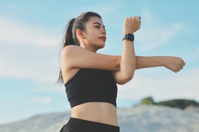 Side view of young woman exercising against sky