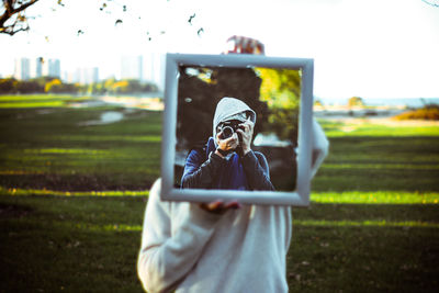 Person holding mirror with reflection of man photographing through camera at park