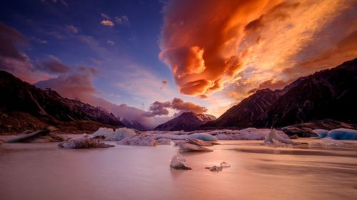 Icebergs in frozen lake against cloudy sky at sunset