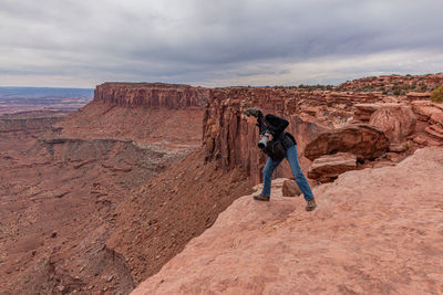 Full frame view of a tourist warily looking over the edge of a rocky cliff