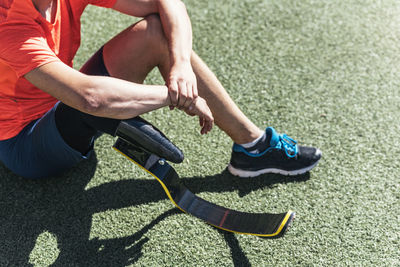 Low section of athlete with prosthetic leg sitting on field against sky