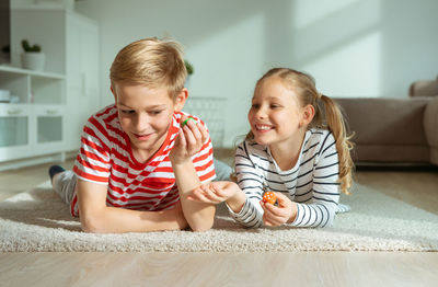 Cheerful siblings playing with dice while lying on carpet at home