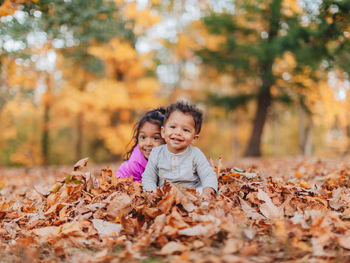 Cute siblings playing while sitting on autumn leaf in forest