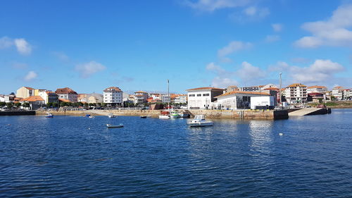 Sailboats in sea by buildings against blue sky