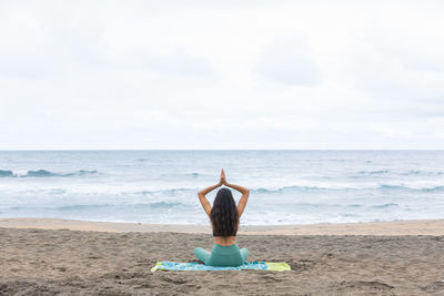 Unrecognizable lady sitting in lotus asana and meditating on beach