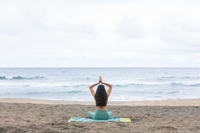 Rear view of woman standing at beach against sky