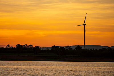Silhouette wind turbine against orange sky