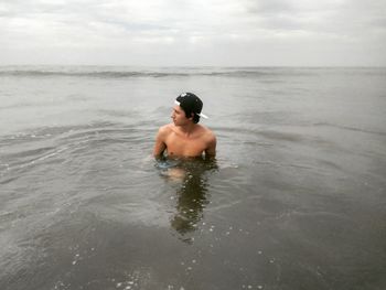 Shirtless young man in sea against sky