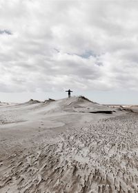 Distant view of man standing on sand dune at desert against cloudy sky