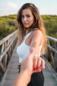 Cropped image of man holding young woman hand on footbridge