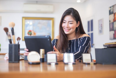 Portrait of a smiling young woman using phone on table