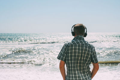 Rear view of man looking at sea against clear sky